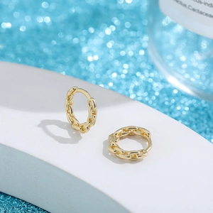 Detalle de pendientes de aro dorados tipo cadena sobre piedra con fondo azul brillante