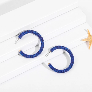 Close-up of blue beaded C-shaped hoop earrings on a white pedestal with a starfish