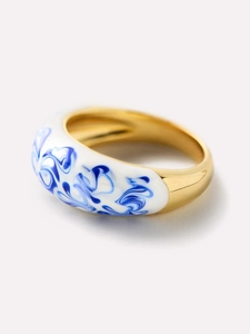 Macro d'une bague dorée en émail blanc avec des motifs en spirales bleues
