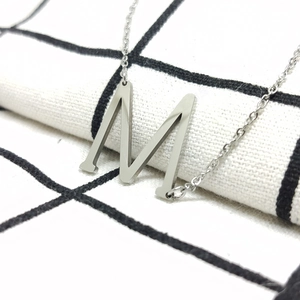 Macro-opname van een minimalistische zilveren letter M-hanger aan een roestvrijstalen ketting