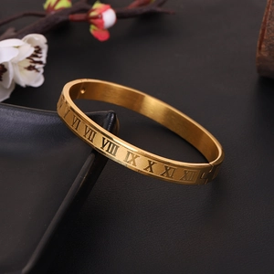 Brushed gold stainless steel bangle featuring engraved Roman numerals on black leather