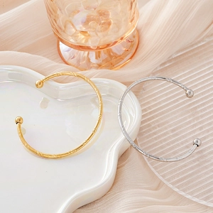 Detailed macro of C-shaped spiral pattern bangles with polished bead ends in gold and silver