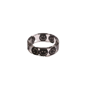 Anillo de resina transparente con motivos de caritas negras sobre un fondo blanco minimalista