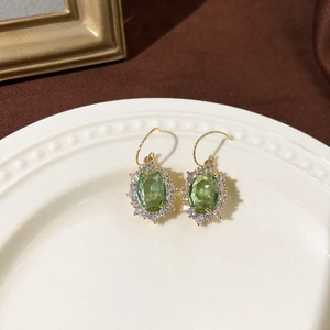 Detailansicht von Vintage-Ohrringen mit smaragdgrünen Steinen und Goldakzenten auf weißem Teller