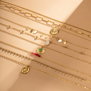 Detail van gelaagde gouden kettingen met zun-hanger, groene stenen en roze kralen