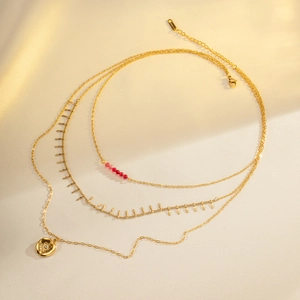 Detail van gouden gelaagde roestvrijstalen ketting met rode kralen en zonnebedel