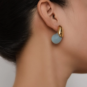Dettaglio di orecchini minimalisti in metallo dorato e resina azzurra sulla modella