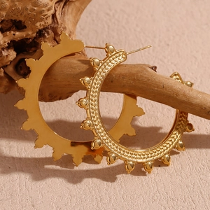 Detail of bohemian gold earrings with wheat ear texture and beaded edge on wood stand