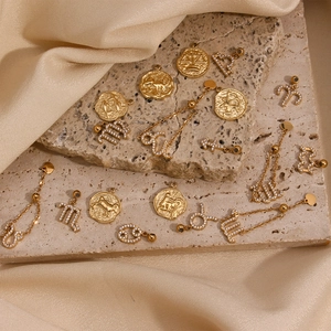 Detail of 18K gold-plated zodiac pendants with rhinestones on stone and silk background