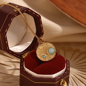 Macro shot of 18K gold starburst compass pendant with blue gems on a red jewelry box