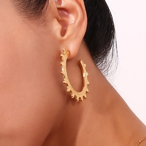 Close-up of golden hoop earrings featuring wheat patterns and boho stud details