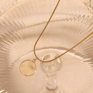 Detailed view of the 18K gold plated compass pendant and snake chain on ribbed glass