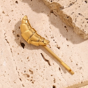 Close-up of 18K gold plated croissant hair clip on a textured beige stone background