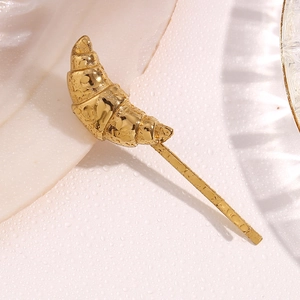 Macro shot of gold horn-shaped hair clip with spiral texture on a wet pink surface