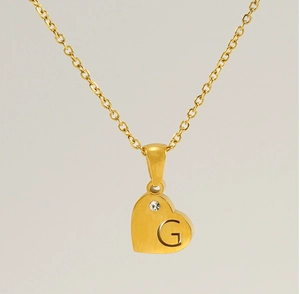 Gros plan d'un collier pendentif cœur doré avec gravure G et petit détail en zircone