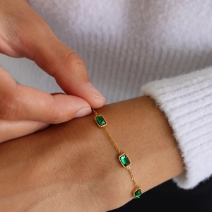 Detailed view of a gold bracelet with three rectangular emerald green stones worn on wrist