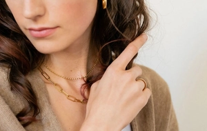 Gros plan de colliers à maillons trombones et boucles d'oreilles dorés 18K sur un mannequin