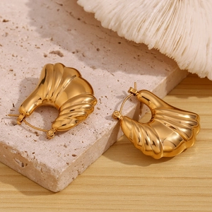 Close-up of gold hollow wing earrings with ribbed texture on a natural stone base