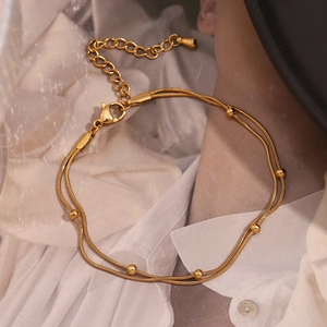 Detailed view of dual-layer gold snake chain anklet with metal beads and drop charm