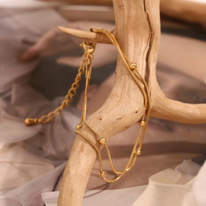 Double-layered gold snake chain anklet with round beads on natural wooden branch