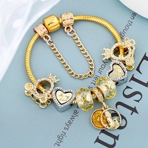Bracciale a serpente dorato con ciondoli a cuore e corona su una rivista azzurra