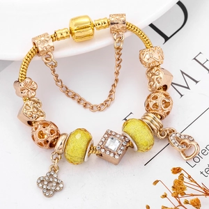 Goldenes Schlangenarmband mit gelben Kristallperlen und Herzanhängern auf weißem Teller