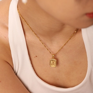Close-up of gold coin necklace with rectangular angel pendant on a female model