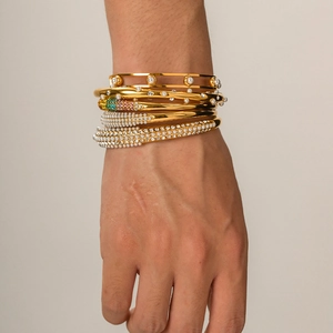 Close-up of stacked gold 18K plated bracelets featuring pearls and colorful rhinestones