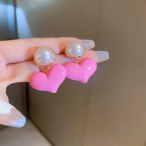 Pink heart drop earrings with white pearl detail and gold border held in hand