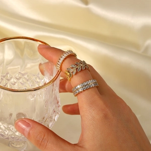 Close-up of three 18K gold-plated rings with zircon stones worn by a hand on silk background