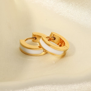 Détail de créoles dorées 18 carats avec émail blanc sur tissu de soie beige