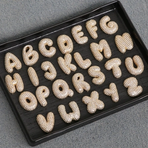 Vue macro de 26 pendentifs alphabet avec zircons sertis sur un plateau à bijoux noir