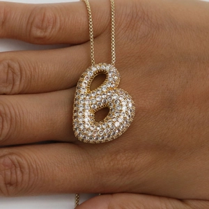 Détail du collier pendentif lettre B dorée avec oxydes de zirconium tenu à la main