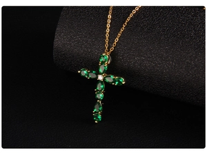 Macro detail of gold cross pendant with vibrant green teardrop cubic zirconia stones