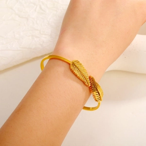 Vista dettagliata di un bracciale aperto a piuma dorata con trama fine sul polso di donna