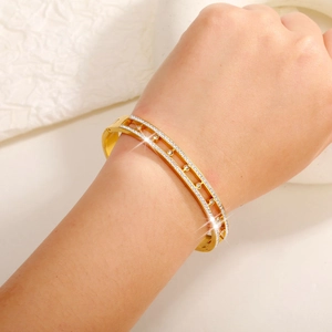 Dettaglio macro del bracciale rigido dorato a doppia fila di cristalli sul polso