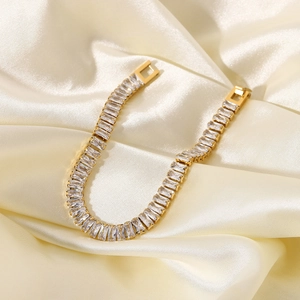 Dettaglio del bracciale dorato con zirconi rettangolari su seta color champagne