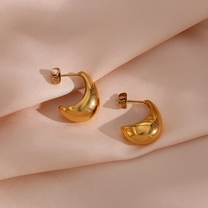 Détail de boucles d'oreilles dorées en goutte d'eau sur satin rose avec reflet miroir