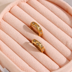 Detail of 18K gold-plated starburst earrings with zircon stones on pink velvet