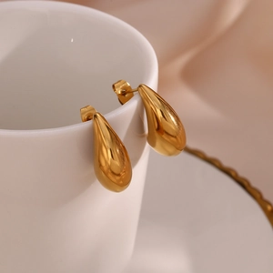 Boucles d'oreilles goutte d'eau dorées polies de forme minimaliste sur une tasse