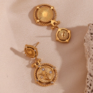 Detail van vintage gouden engel-munt oorbellen met strassteentjes op beige zijde