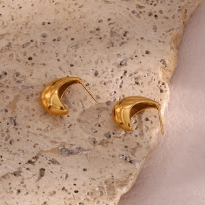 Vue macro de boucles d'oreilles croissants dorées 18K sur pierre texturée