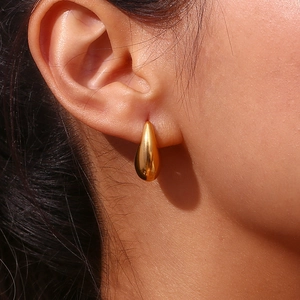 Détail macro d'une boucle d'oreille goutte dorée polie avec fini miroir et rendu porté