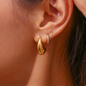 Détail d'une boucle d'oreille goutte dorée et d'un anneau de cristal sur l'oreille