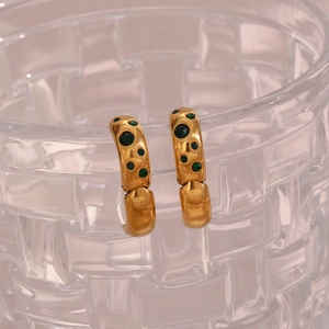 Detailed view of gold-plated hammered C-shaped earrings with green enamel dots on glass