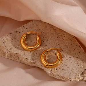 Dettaglio di orecchini a cerchio spessi placcati oro 18K su una superficie in pietra