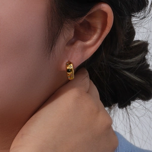 Close-up of gold hoop earrings with multi-colored zircon stones worn by a model