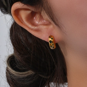 Close-up of gold chunky hoop earring with irregular texture and green gemstone