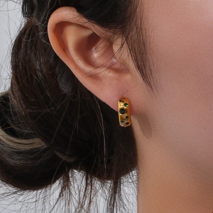 Close-up of chunky gold hoop earring with textured organic surface and green zircon stones