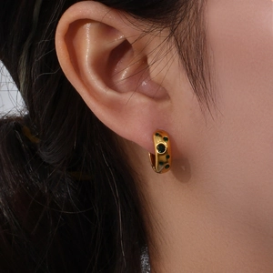 Close-up of gold chunky hoop earrings inlaid with green round zircons on model